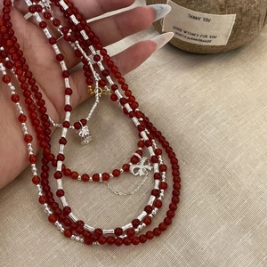 Close-up of red agate beaded necklace with silver tubes and delicate bow pendant charm