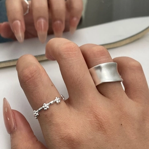 Detail view of a matte silver minimalist wide band and a delicate five-petal flower ring