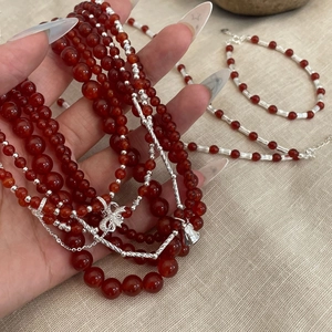 Detail of red agate bead necklace and bracelet with silver bow charms on fabric