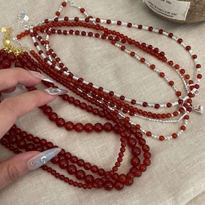 Close-up of layered red agate bead necklace with metallic spacers on linen background