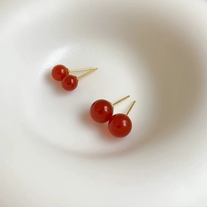 Detail of elegant red agate stud earrings with gold pins in two sizes on white surface