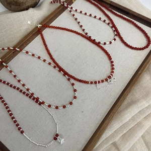 Detailed close-up of red agate beaded necklaces with silver rose and bow pendants