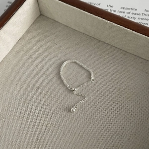 Minimalist adjustable silver tassel ring with textured chain details on linen display