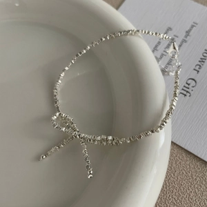 Detail of silver bow pendant and textured crushed bead chain necklace on ceramic plate