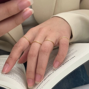 Detailed view of four thin gold rings with textured surfaces worn in a layered style
