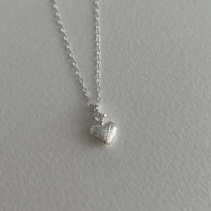 Dettaglio macro del ciondolo a cuore in argento S925 con superficie testurizzata e zircone