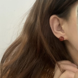 Macro side view of an 8mm red agate spherical stud earring worn on a model earlobe