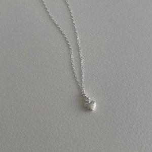 Dettaglio macro della collana a cuore argento con zircone e trama in metallo spazzolato