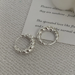Gros plan de boucles d'oreilles créoles torsadées en argent sur un fond en tissu blanc