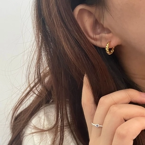 Détail d'une boucle d'oreille torsadée dorée et d'une bague minimaliste en argent avec gemme