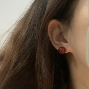 Macro close-up of a deep red agate stud earring worn on a model's ear for casual style