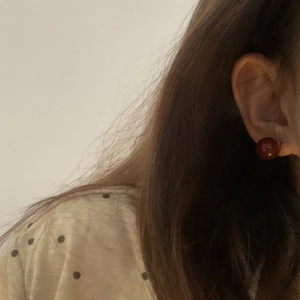 Macro side view of a minimalist round red agate stud earring on a person's ear