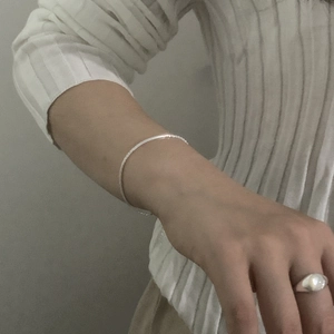 Detail of a minimalist S925 sterling silver chain bracelet on model with a white ring