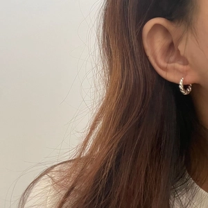 Détail de créoles en argent S925 avec texture torsadée portées sur l'oreille du modèle