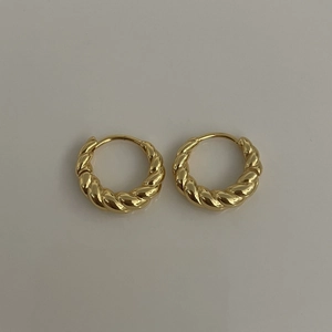 Détail de boucles d'oreilles créoles torsadées dorées avec texture spirale polie