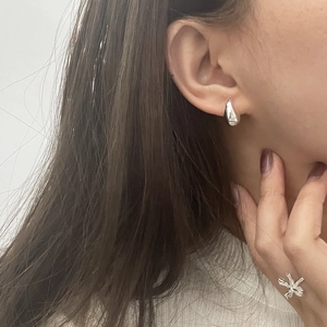 Macro view of teardrop silver stud earrings and flower ring worn by a female model