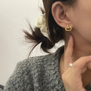 Close-up of a minimalist hollow heart gold stud earring worn by a model in casual setting