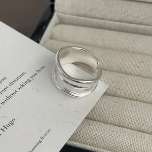 Detailed close-up of a silver-colored wide layered ring with linear texture on fabric