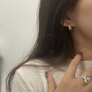 Close-up of elegant gold teardrop earrings and silver ribbon ring on a model