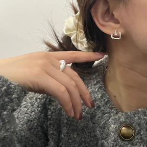 Detail of S925 silver hollow heart earring and textured woven ring on a female model