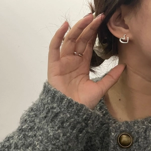 Close-up of minimalist silver heart studs and a thin open ring worn by a model
