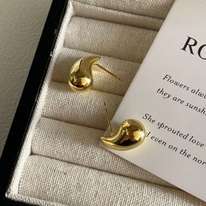 Macro shot of polished gold-plated teardrop earrings on minimalist velvet display