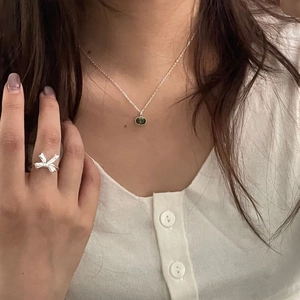Detailed view of 925 silver necklace with green gem and bow ring on a model