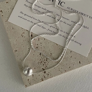 Gros plan d'un collier argenté double couche avec une perle mate brossée sur travertin