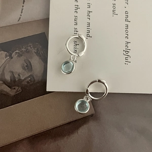 Detailed view of silver hoop earrings with round light blue stones on vintage paper