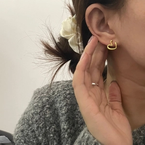 Close-up of a model wearing minimalist golden heart-shaped earrings on a white backdrop