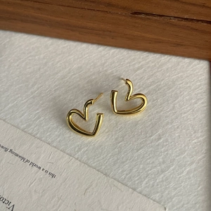 Detailed close-up of gold minimalist hollow heart earrings on a white textured card