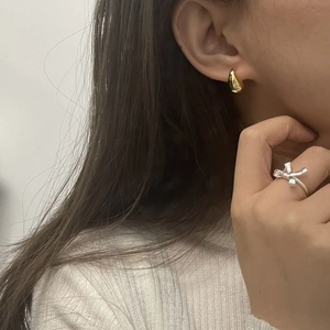 Detailed view of teardrop gold earrings and a silver bow ring on a female model