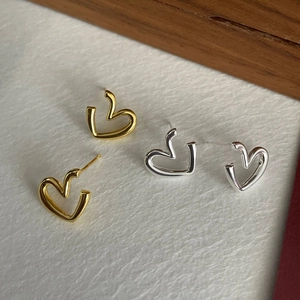 Close-up of minimalist gold and silver hollow heart earrings on textured paper