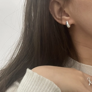 Close-up of polished silver teardrop earrings on a model with a minimalist bow ring