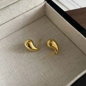 Macro detail of high-polish gold teardrop earrings inside a minimalist beige jewelry box