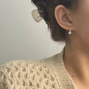 Close-up of S925 sterling silver drop earring with round light blue gemstone on ear