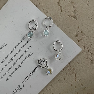 Macro view of silver S925 earrings with blue and clear gemstones on white paper