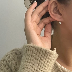 Close-up of minimalist silver round pendant stud earrings worn with a beige sweater