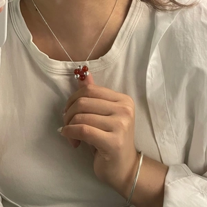 Close-up of S925 silver necklace with red bead floral pendant on a white t-shirt