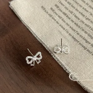 Boucles d'oreilles nœud en argent S925 avec zircons scintillants sur fond lin rustique