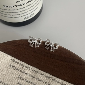 Détail de boucles d'oreilles nœud en argent S925 avec zircons sur socle en bois