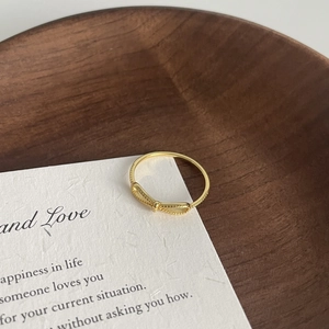 Macro shot of gold minimalist twist ring band resting on a textured white card background