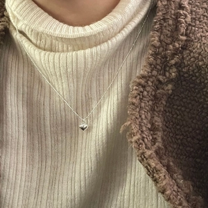 Gros plan d'un collier cœur en argent sterling S925 porté avec une tenue d'hiver douillette
