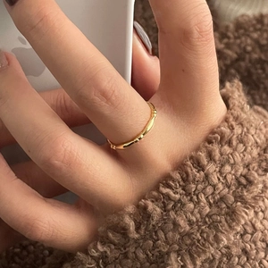 Detail of a minimalist gold bamboo style ring on a finger in a lifestyle setting