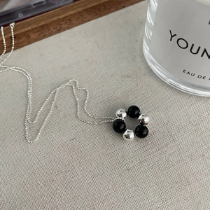 Detailed view of S925 silver necklace with black and silver beads on a beige texture