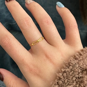 Close-up of a minimalist gold bow ring with textured finish on a person's hand