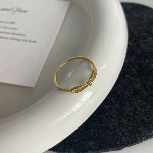 Detail of a minimalist gold bow ring with delicate beaded edges on a ceramic display