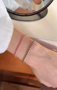 Detail of red and black braided bracelets with small metal beads on wrist in natural light