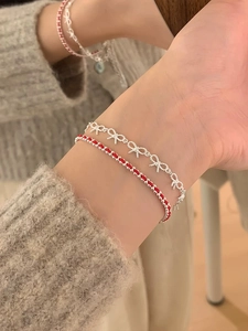 Close-up of S925 sterling silver bow chain and red woven bracelet set on wrist