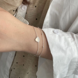 Détail du bracelet double couche en argent 925 avec pierre en cœur sur le poignet d'une femme